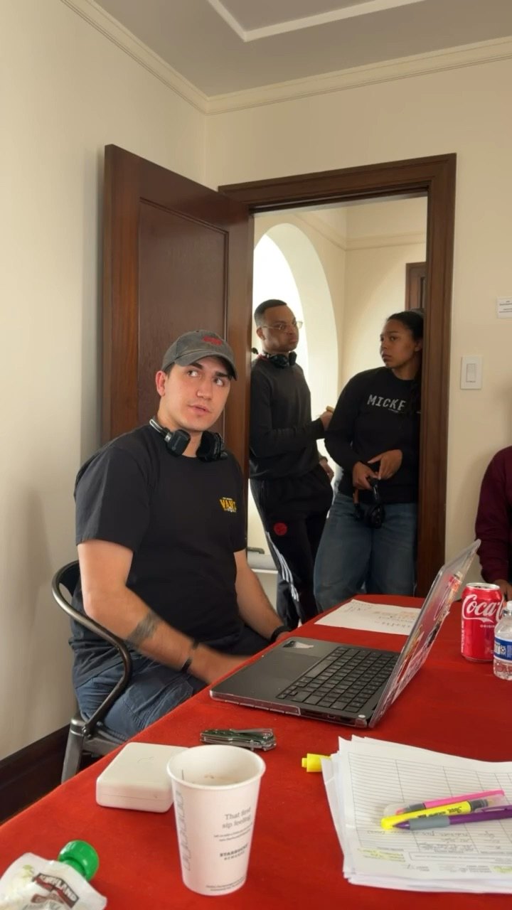 Joel Cazares at the production table on set, laptop open, with crew standing in the doorway behind him.